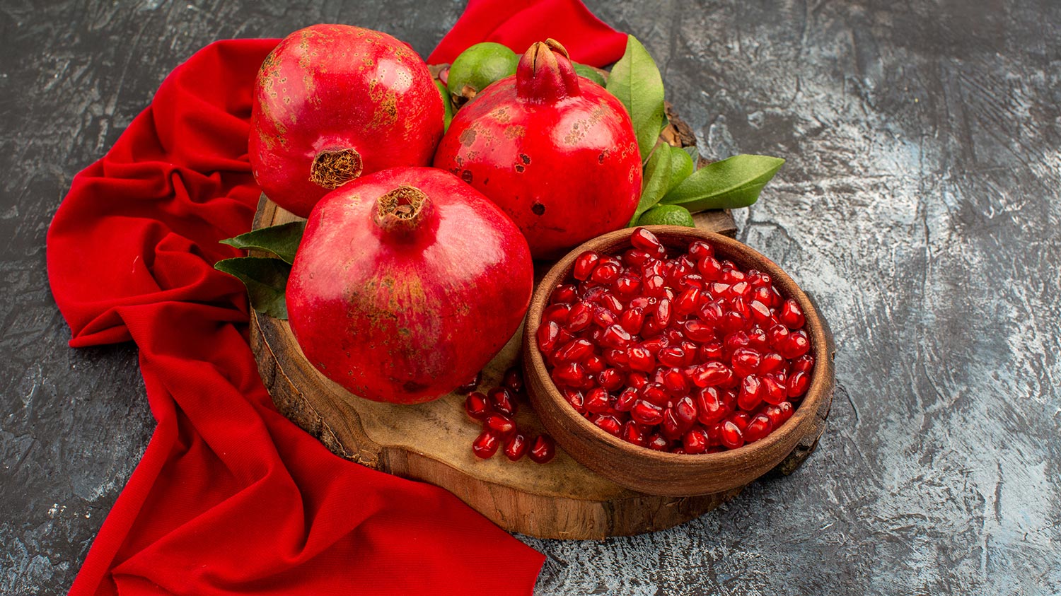 تصویر انار و برگ و پارچه قرمز بر روی میز